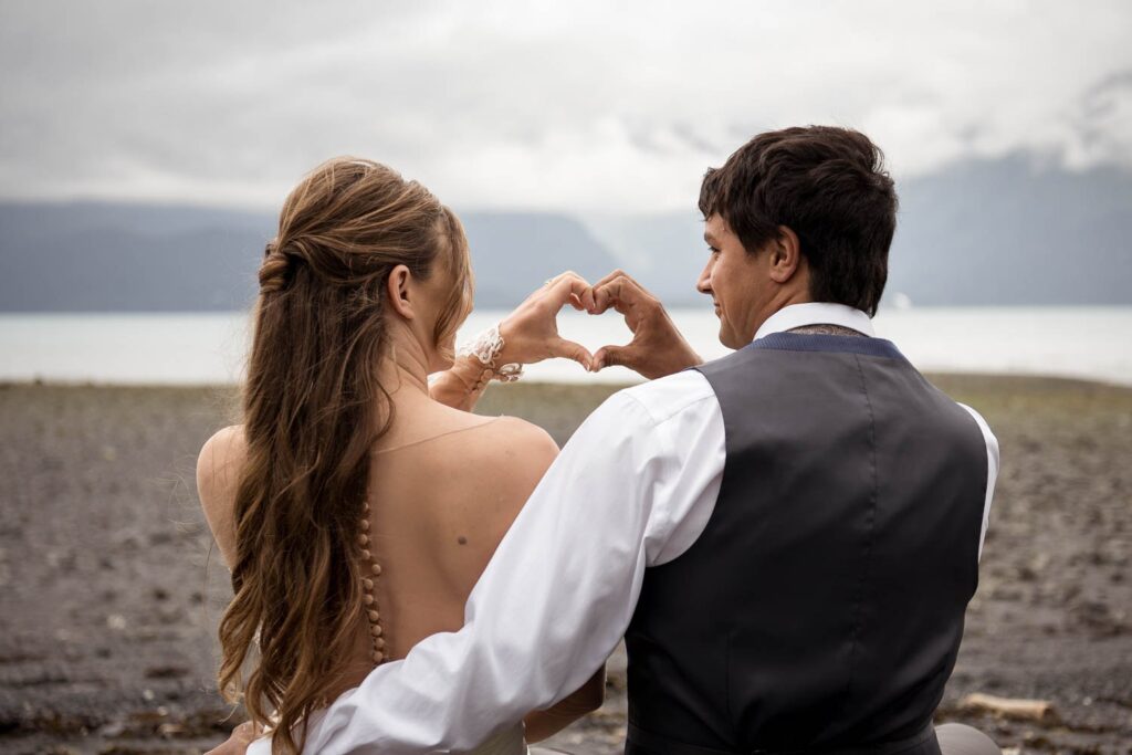 Bride and groom make heart hands during a beach elopement in Seward, Alaska