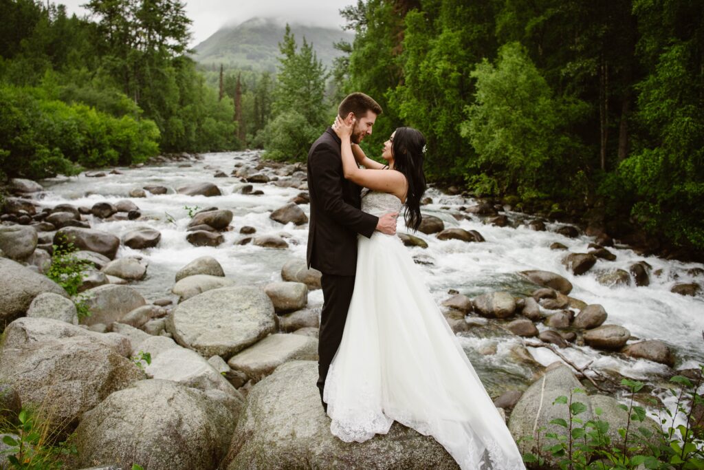 Hispanic bride with groom on boulders along a mountain river in Palmer, Alaska