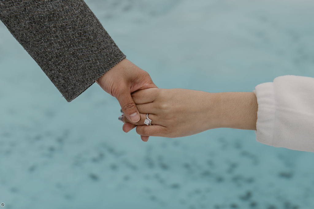 Hands with an engagement ring over a glacier pool